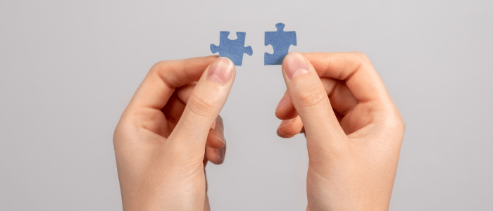Two hands each holding small blue puzzle pieces, to represent the concept that Every Cure and Atropos Health are uniting for RWD-driven drug repurposing