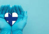 Pair of hands in medical latex gloves hold a heart painted with the flag of Finland, to represent the concept that the FinOMOP consortium uses OMOP CDM for RWD studies milestone