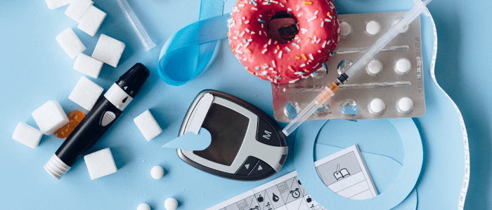 A blood glucose monitor, various tablets, sugar cubes and a pink doughnut on a blue background, to represent the concept of a new report that explores real-world data trends in GLP-1 RA medications