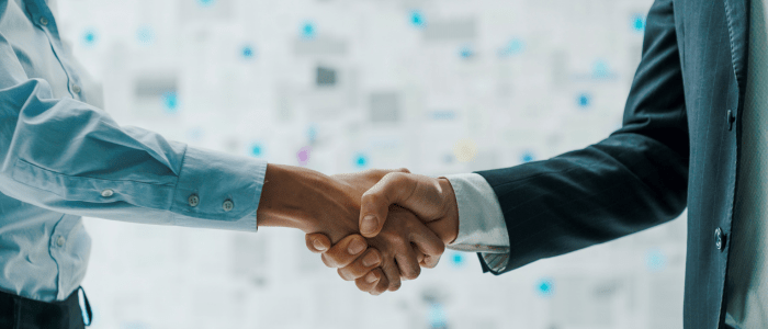 Two people shaking hands in front of a blurry background. One person is in a suit, one is in a shirt. They are only visible from their waist to their shoulders. To represent that Flatiron and NCCN to improve cancer outcomes using RWD.
