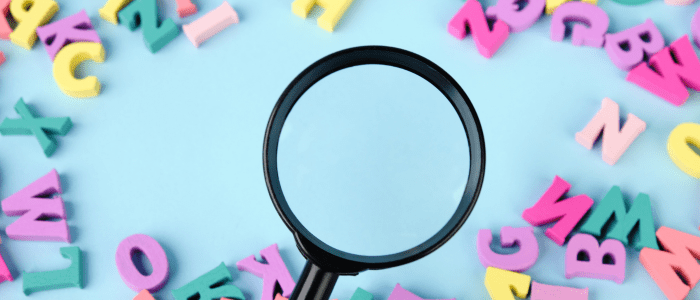 A magnifying glass looking at brightly coloured plastic letters on a light blue background. To represent that FDA and NIH announce glossary for clinical and RWE research.